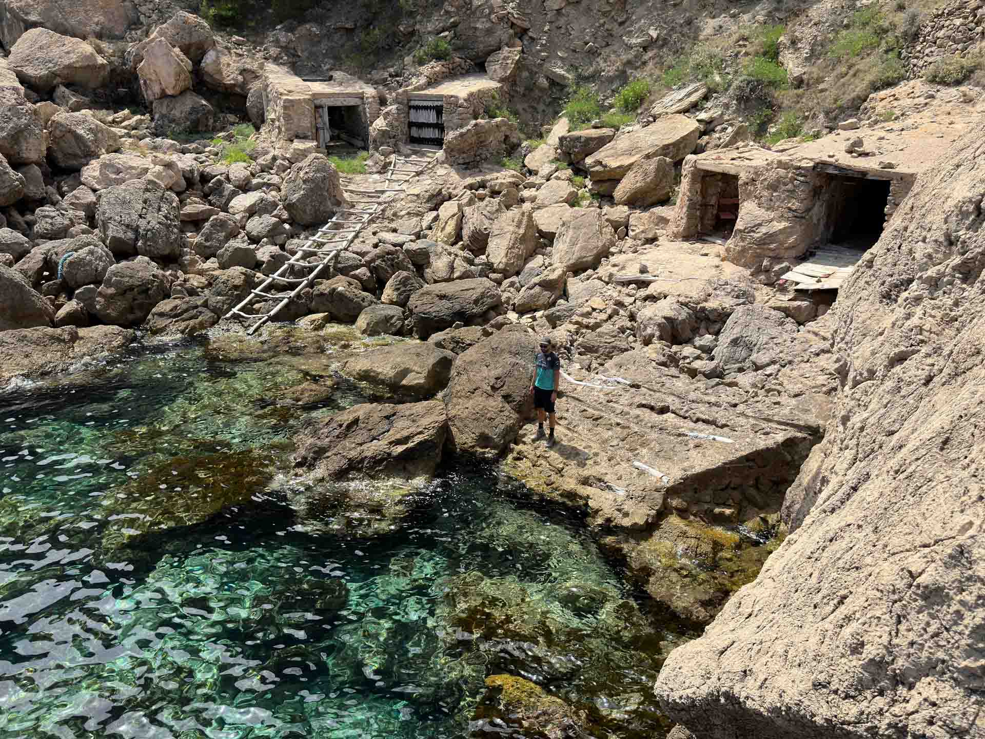 View of a hidden cove with turquoise waters surrounded by rocky cliffs and forest, showcasing one of Ibiza’s remote natural swimming spots