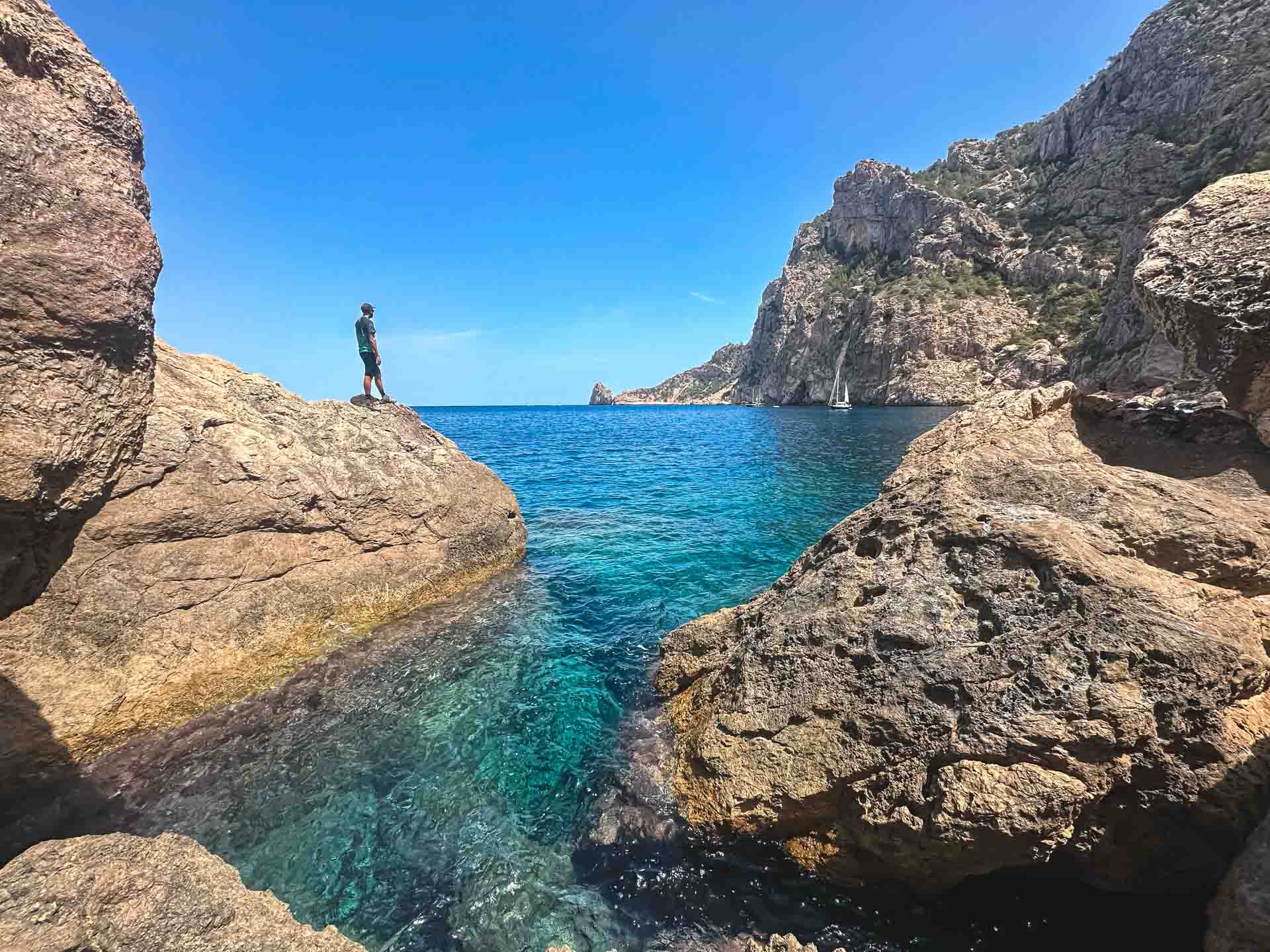 Hikers standing on a mountain ridge overlooking the turquoise sea of Ibiza and a remote, abandoned cove nestled along the rugged coastline.