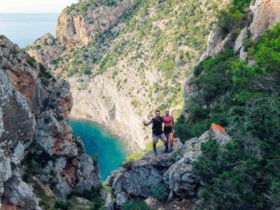 Panoramic view from a cliffside trail overlooking Ibiza’s rugged coastline and turquoise sea, with hikers pausing to admire the scenery on their way to a secret cove.