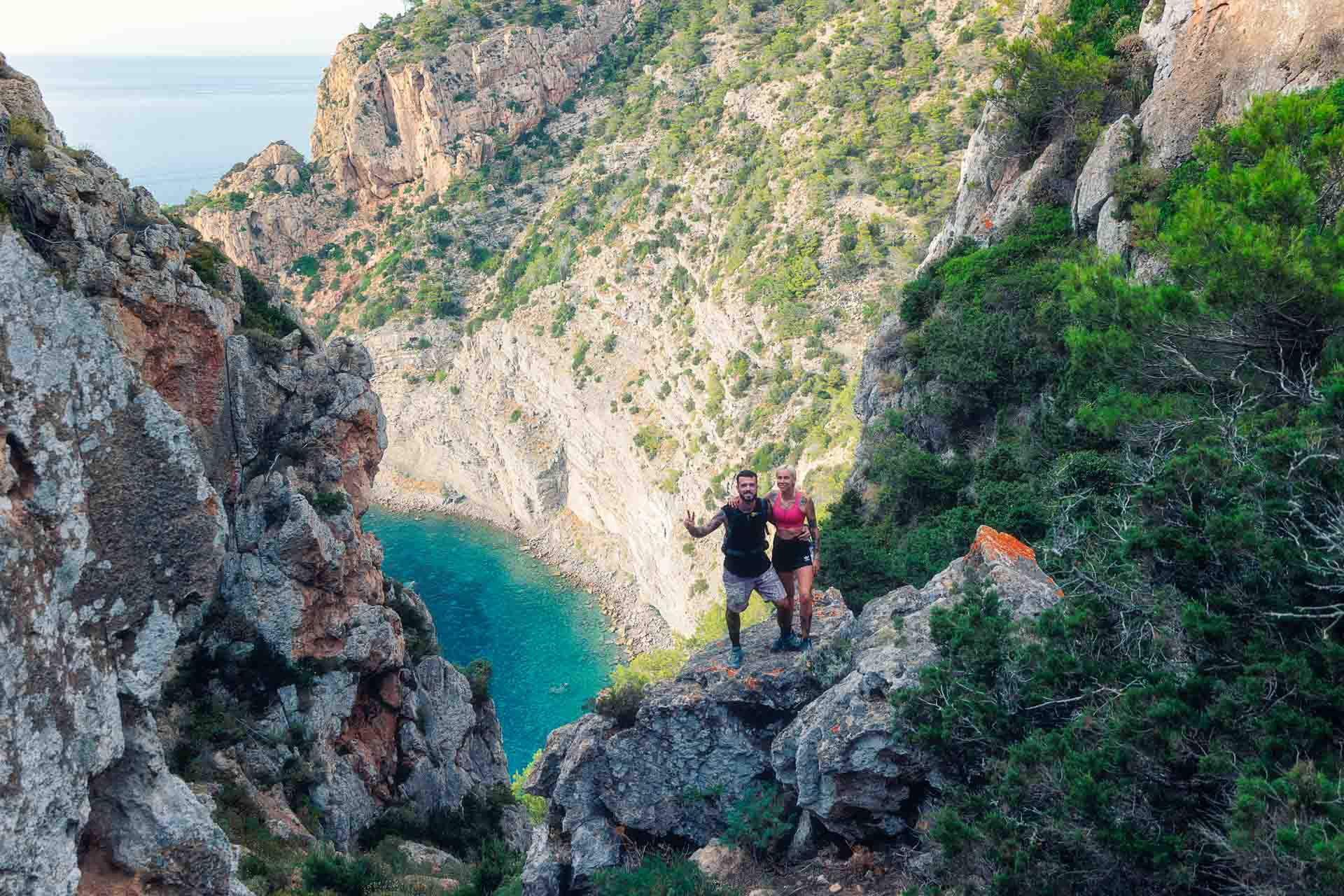 Panoramic view from a cliffside trail overlooking Ibiza’s rugged coastline and turquoise sea, with hikers pausing to admire the scenery on their way to a secret cove.