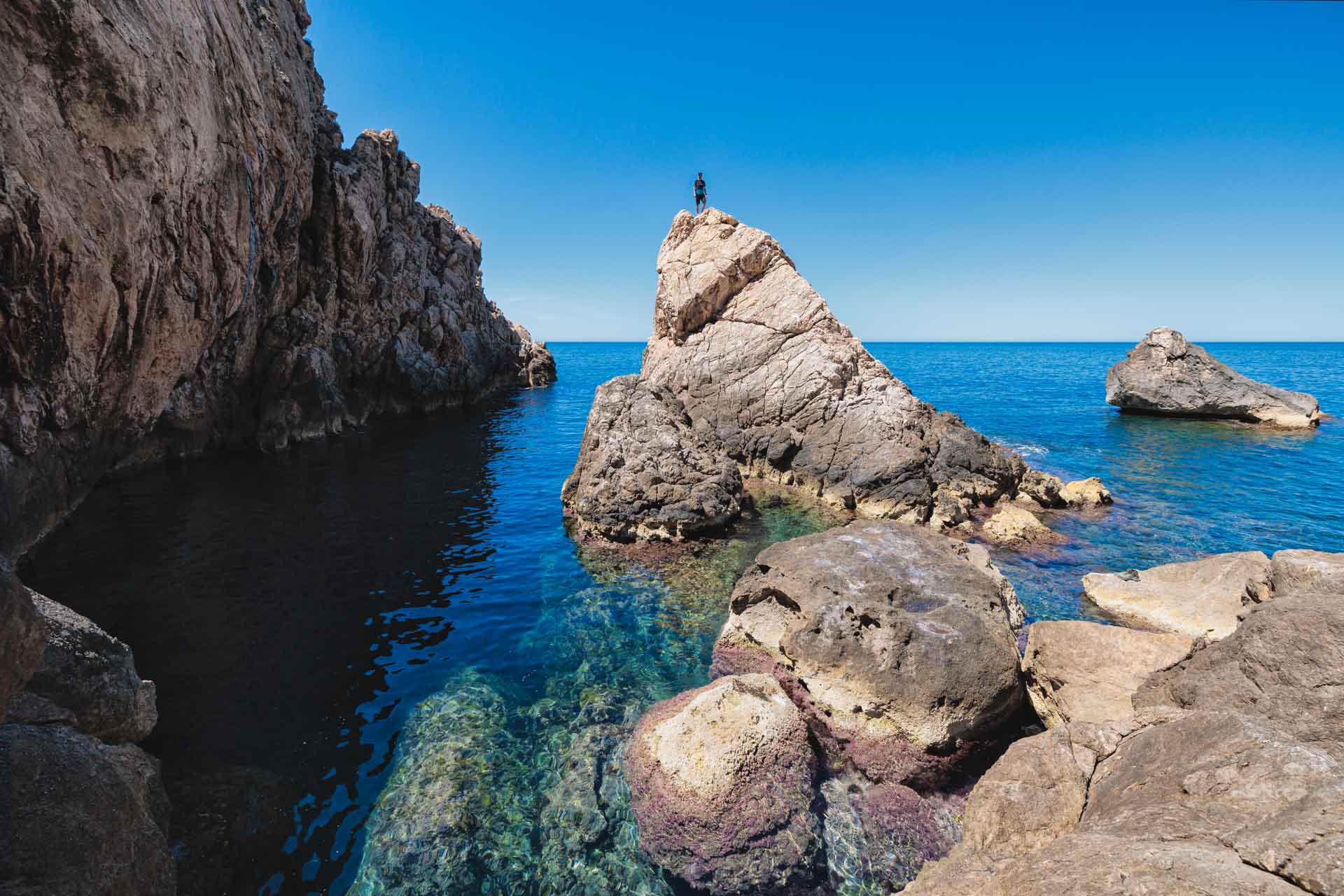 A hidden cove on Ibiza’s wild coast, where timeworn huts meet crystal-clear sea and silence echoes between cliffs and forested paths.