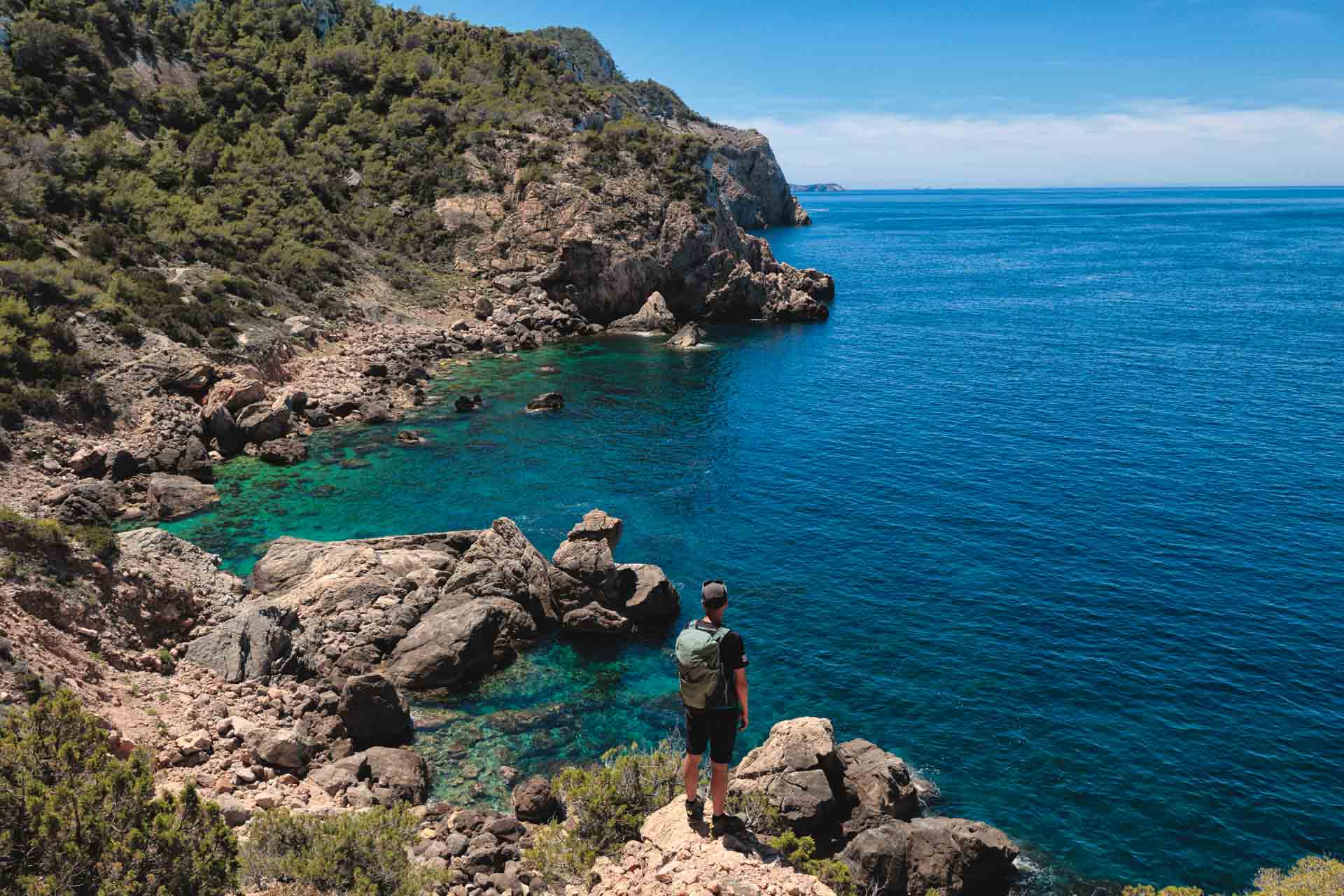 Secluded cove in Ibiza with turquoise water and abandoned fishermen’s huts, surrounded by cliffs.
